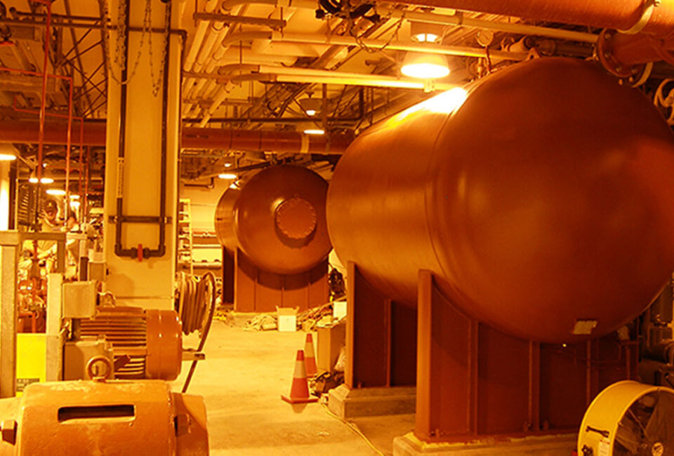 boiler room with large orange tanks and various pipes and equipment in industrial setting