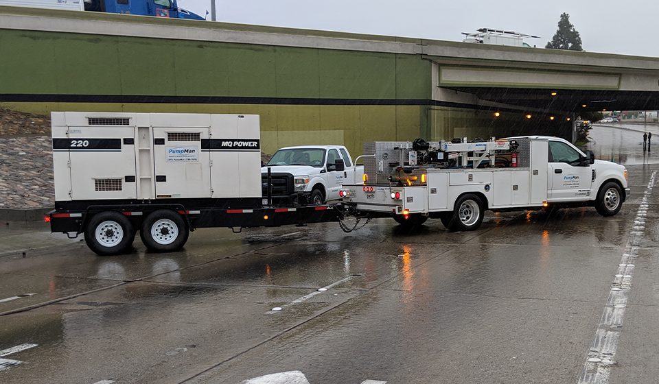 220-volt portable generator with the label MQ Power and PumpMan, being towed by a Ford F-550 service truck from PumpMan