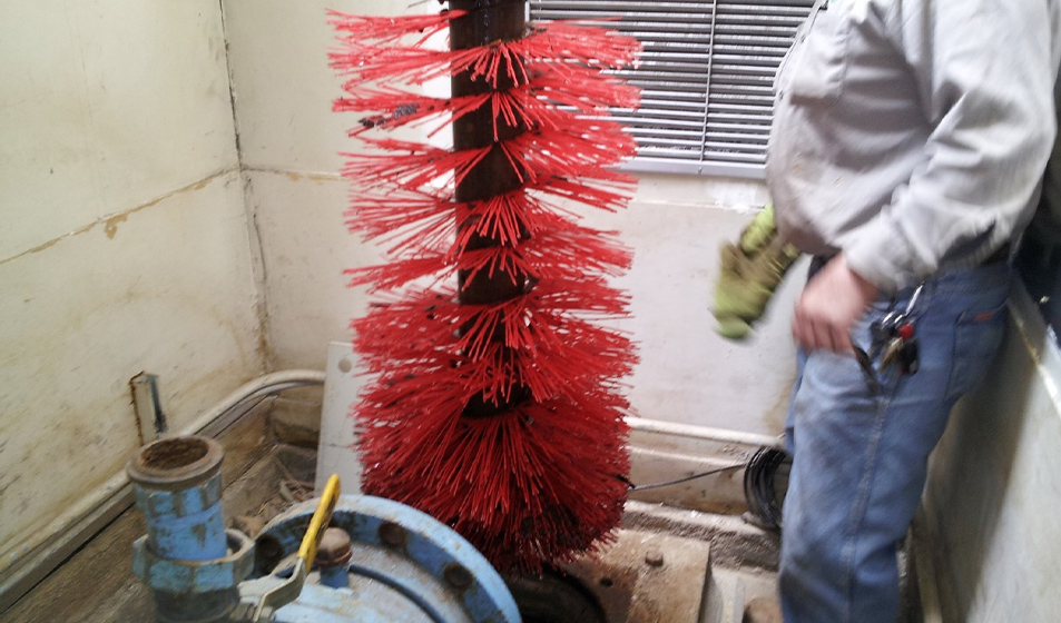 worker standing next to a large, cylindrical brush with red bristles, used for cleaning or industrial applications